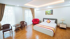 A hotel room with a large bed, a small table, two chairs, a nightstand, and a painting on the wall. - Bao Long Go Vap Hotel (Ho Chi Minh City)