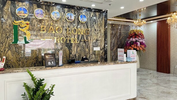 A hotel reception desk with a marble wall, a large chandelier, and a floral arrangement. - Bao Long Go Vap Hotel (Ho Chi Minh City)