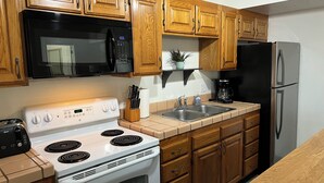 A kitchen with wooden cabinets, a microwave, a stove, a refrigerator, and a coffee maker.