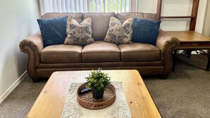 A brown leather sofa with floral-patterned cushions, a wooden coffee table with a potted plant, and a wicker basket.