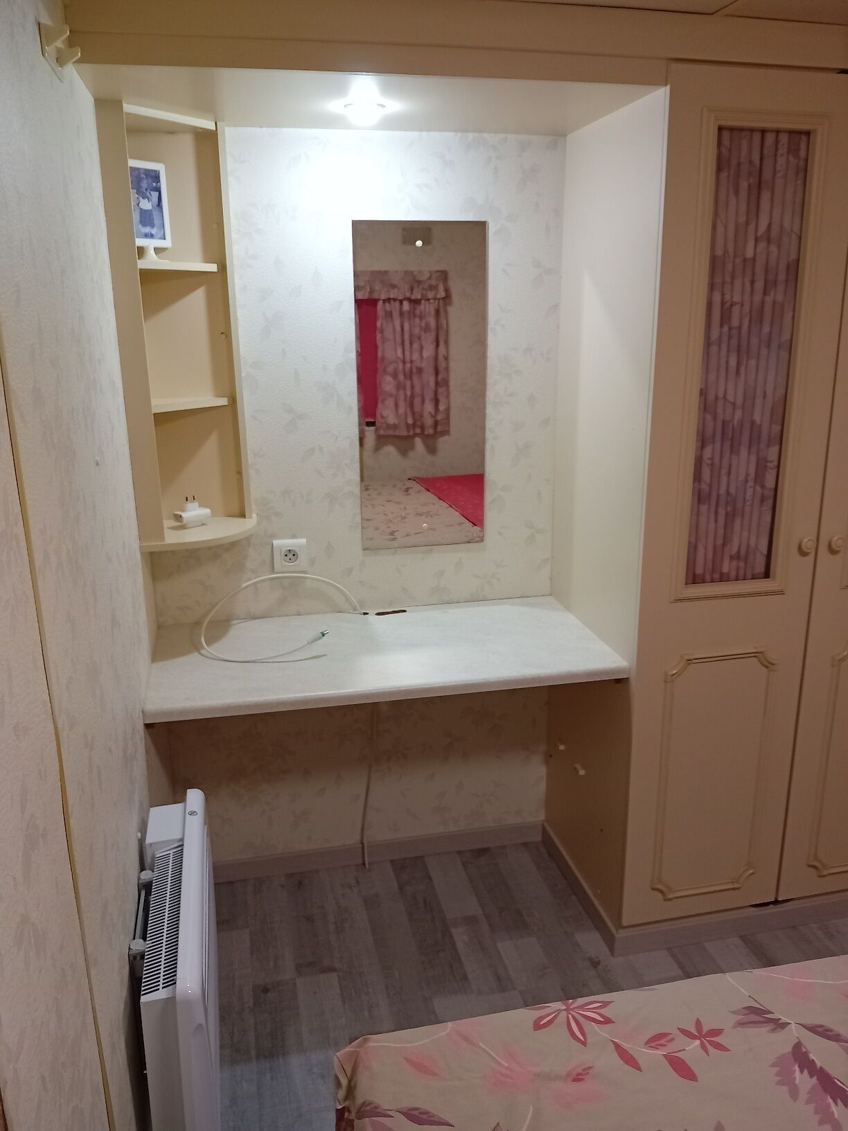 Een kleine kamer met een inbouwkast, een spiegel, een radiator en een kledingkast.