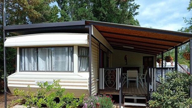 En campingvogn med overdækket veranda, en lille have og et synligt vindue.