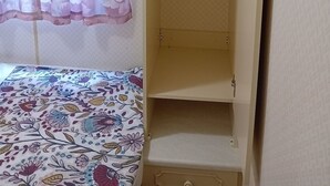 Et værelse med en seng, et garderobeskab med plads til at hænge tøj, og et vindue med blomstrede gardiner.