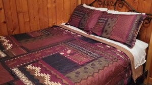 A wooden-paneled room with a bed featuring a patterned bedspread and matching pillows. - Rustic cabin getaway on the shore of Soo Lake in Phillips, WI (Phillips)
