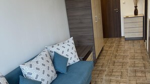 A modern living room with a sofa, patterned cushions, a wooden wardrobe, and a tiled floor.