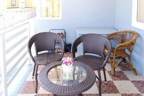 Een balkon met rieten stoelen, een glazen tafel met een vaas en een schoenenrek.