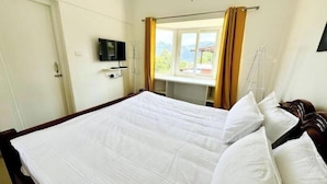 A hotel room with a large bed, a television mounted on the wall, and a window with curtains.
