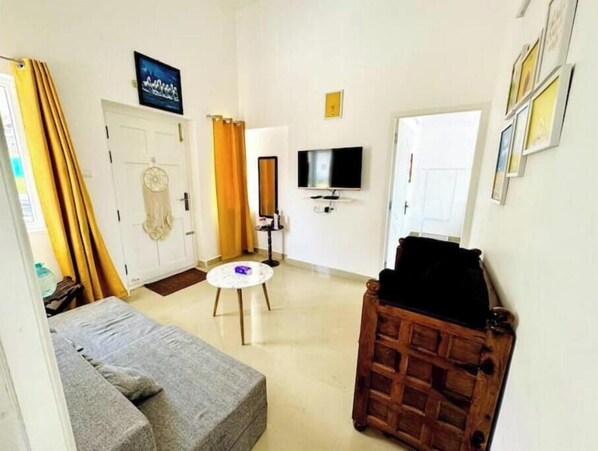Een woonkamer met een grijze bank, een ronde salontafel, een houten kast, een televisie en een deur voorzien van een gordijn.