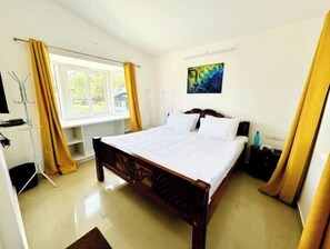 Een slaapkamer met een houten bed, een raam met gele gordijnen en een schilderij aan de muur.