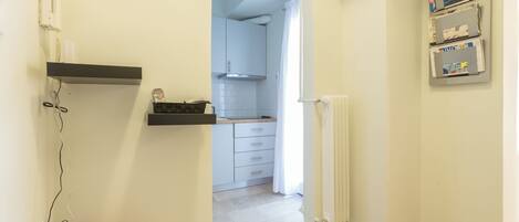 A hallway leading to a kitchen with a fire extinguisher, a radiator, and a shelf with magazines.
