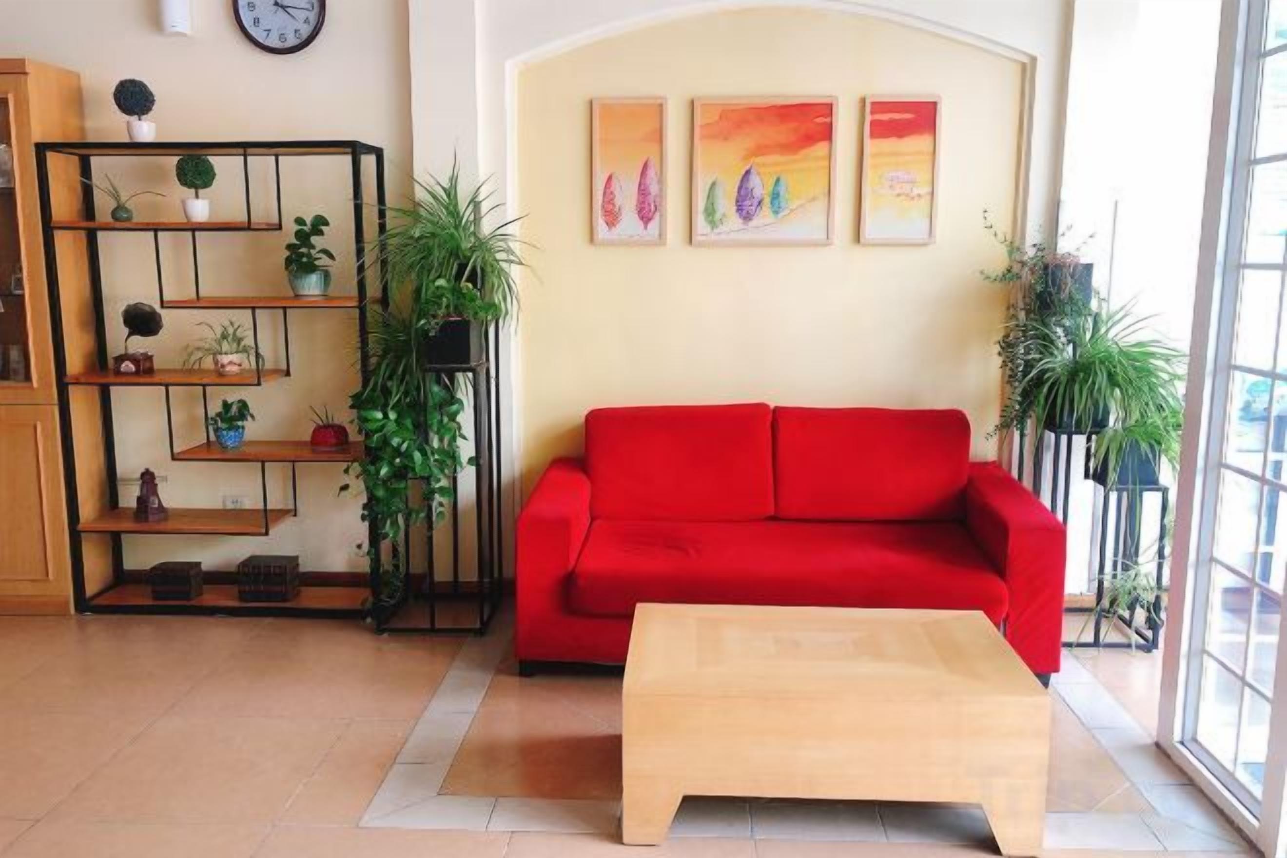 A living room with a red sofa, a wooden coffee table, and a bookshelf with plants.