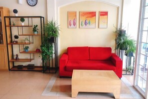 Een woonkamer met een rode bank, een houten salontafel en een boekenkast met planten.