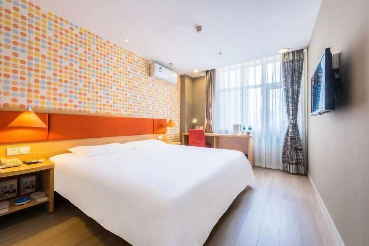 A hotel room with a large bed, a desk, a TV, and a window with curtains.