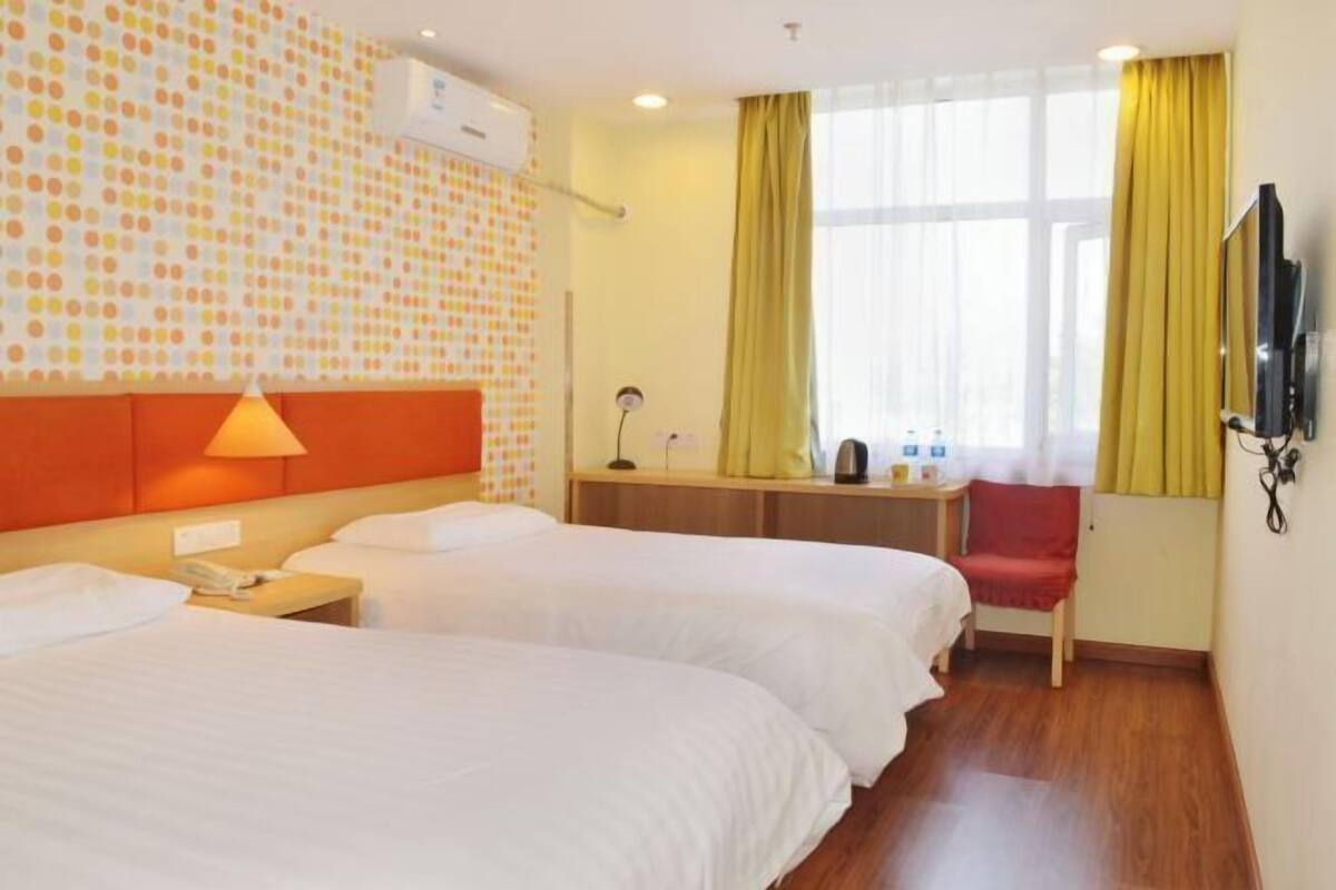 A hotel room with two beds, a desk, a TV, and a window with curtains.