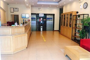 Een hotel lobby met een receptiebalie, een rode bank, een houten kast en een plant.