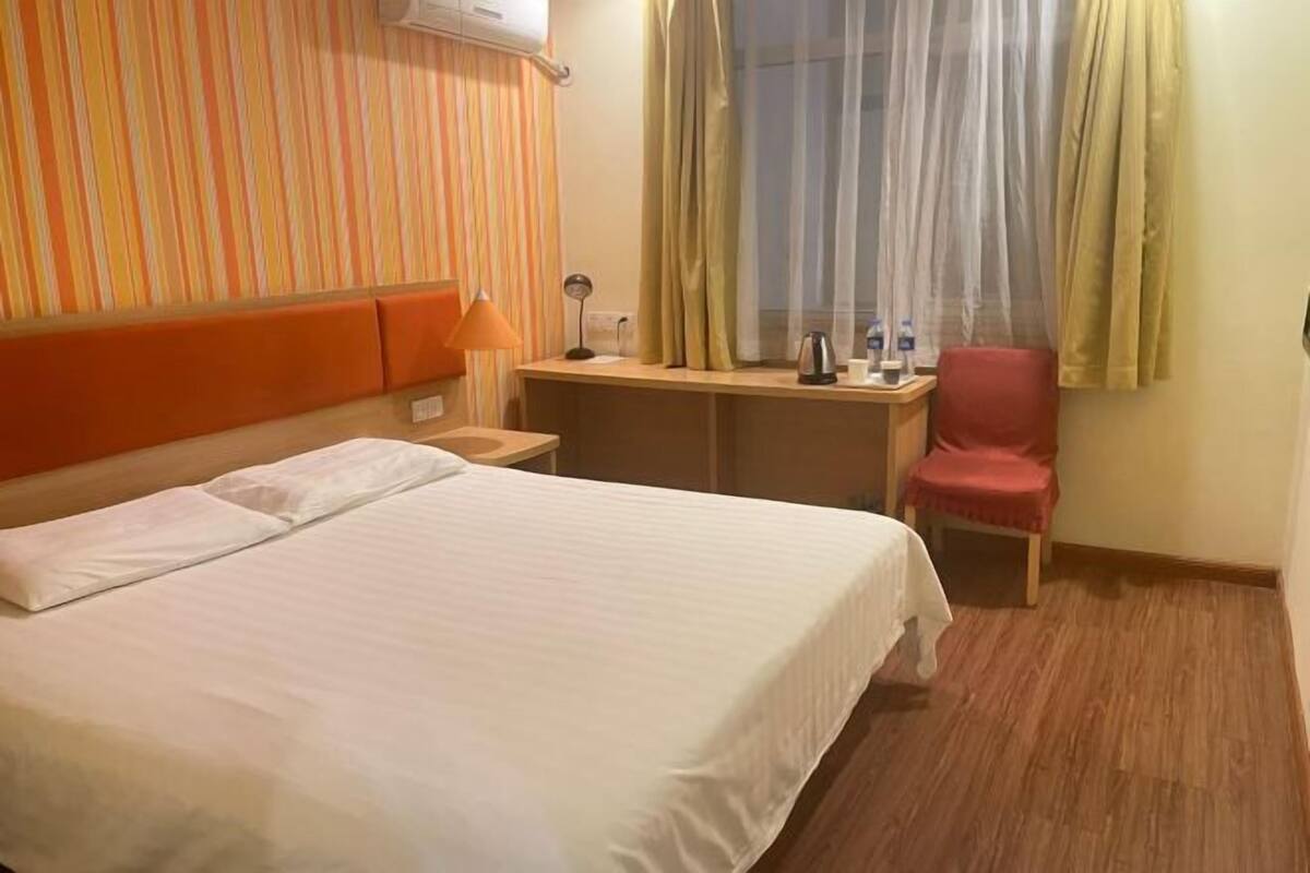 A hotel room with a bed, a desk, a chair, and a window with curtains.
