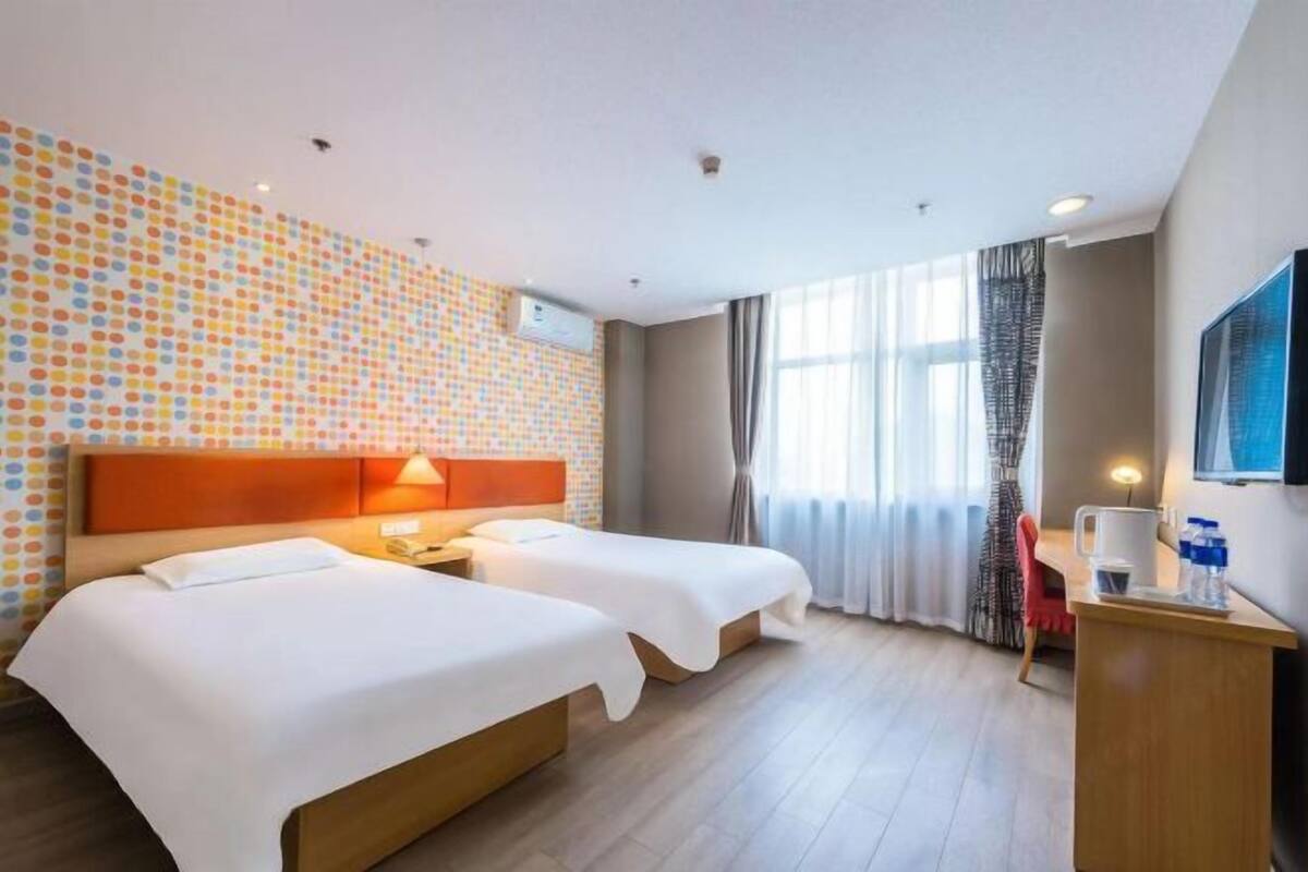 A hotel room with two beds, a desk, a TV, and a patterned wall.