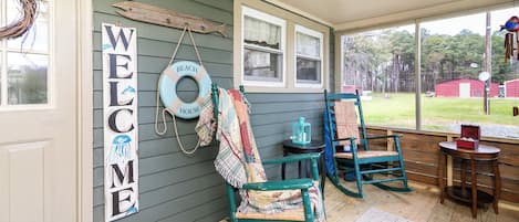 Une véranda avec des fauteuils à bascule, une pancarte de bienvenue et une décoration sur le thème de la plage.