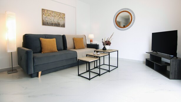 A modern living room with a grey sofa, two coffee tables, a TV stand, and a wall-mounted mirror. - Phaedrus Living: Skiathos Luxury Residences Lime (Skiathos)
