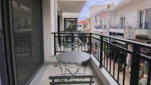 A balcony with a table and chairs, a view of the street, and a building with a sign. - Phaedrus Living: Skiathos Luxury Residences Lime (Skiathos)