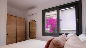 A bedroom with a bed, a wardrobe, and a window with a view of pink flowers. - Phaedrus Living: Skiathos Luxury Residences Lime (Skiathos)