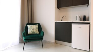A compact living space with a green armchair, a small white refrigerator, and a kitchen area with a sink and coffee maker. - Phaedrus Living: Skiathos Luxury Residences Lime (Skiathos)
