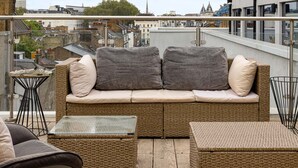 Eine Dachterrasse mit Korbausstattung, zwei Beistelltischen und einem Glastisch.