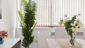 Ein Essbereich mit weißem Tisch, Stühlen, einer Topfpflanze und einer Vase mit Blumen.