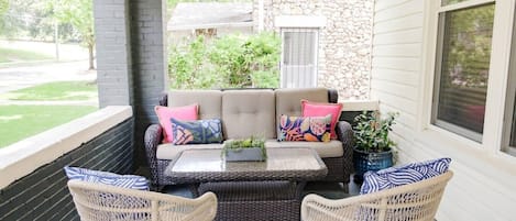 A covered porch with a wicker sofa set, two wicker chairs, and a small table.