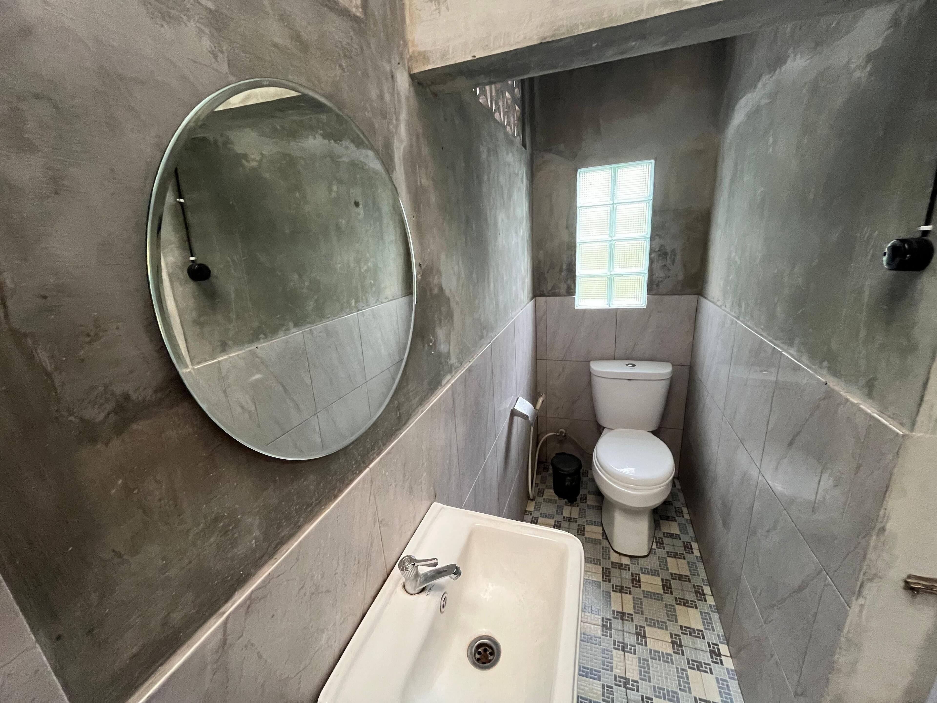 Een badkamer met een ronde spiegel, een wastafel, een toilet en een klein raam.