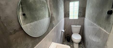 Een badkamer met een ronde spiegel, een wastafel, een toilet en een klein raam.