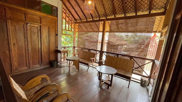 Habitaci ón con suelo de madera, techo de paja, muebles de madera y vistas a través de una celosía de bambú.
