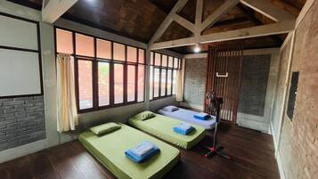 A room with two single beds, a wooden ceiling, brick walls, and large windows.