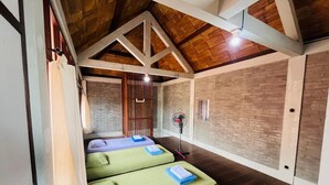 Una habitación con dos camas, un ventilador, una pared de ladrillo y vigas de madera.