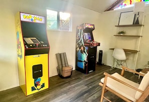 A room with two arcade machines, a white chair, and a small table.