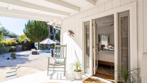 A covered patio with a white chair, a potted plant, and a door leading to a bedroom. - Heated pool, hot tub, arcade, walk to town (Los Alamos)