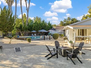A backyard with a pool, lounge chairs, and a covered seating area.