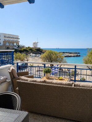 A balcony with wicker furniture, a view of the sea, a windmill, and a building with a sign. - Stelios' Beachfront Retreat (Paroikia)