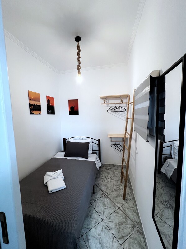 A small, neatly arranged bedroom with a single bed, a small desk with a chair, and a ladder. There are three framed pictures on the wall. - Stelios' Beachfront Retreat (Paroikia)