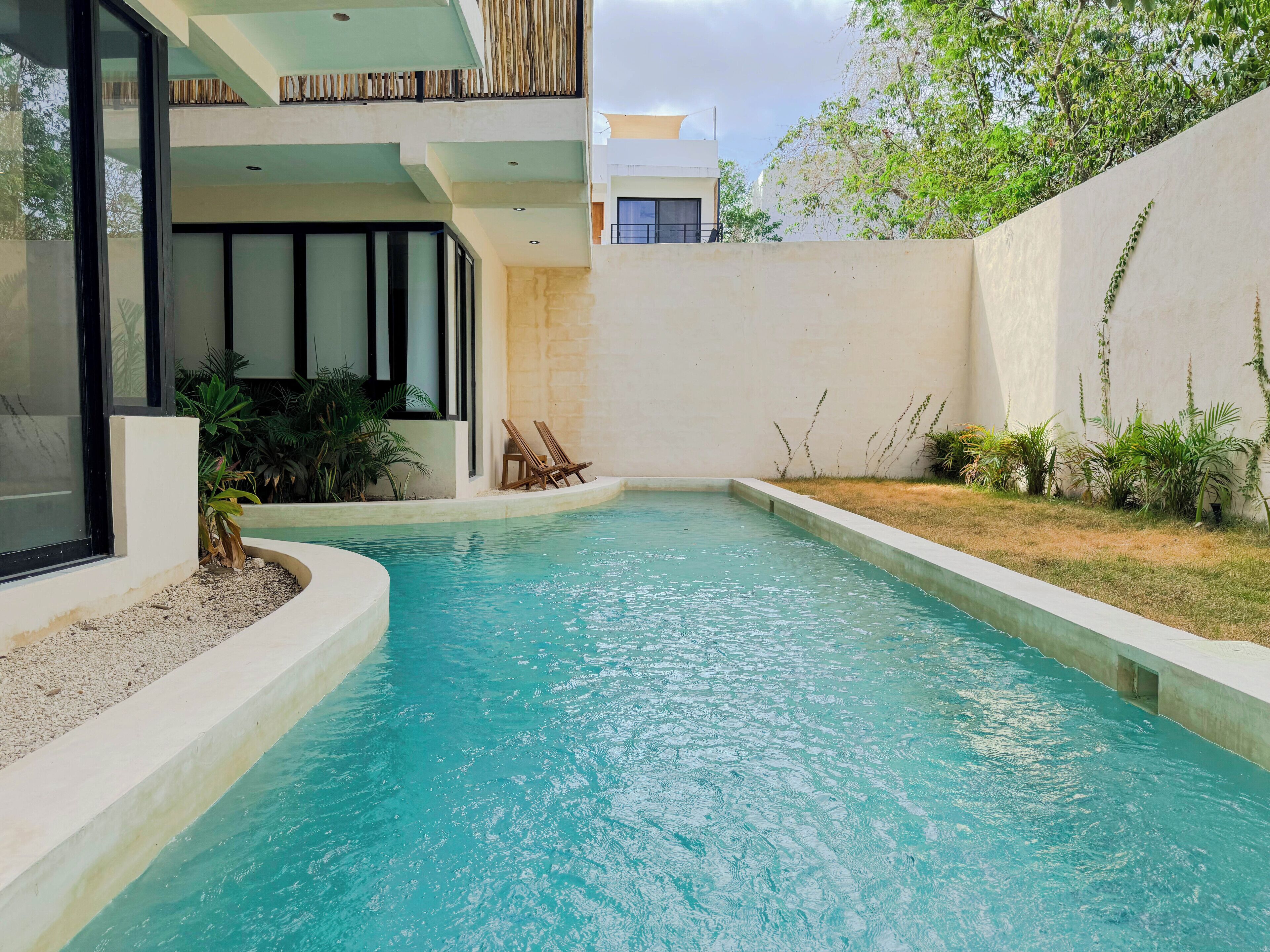 Una piscina con dos sillas de madera, rodeada por un muro bajo y plantas.