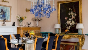 Ein formeller Speisesaal mit einer Kristallleuchter, einem großen Blumenbild und einem goldgerahmten Spiegel.