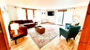 Ein geräumiges Wohnzimmer mit einem braunen Sofa, einem blauen Sessel, einem Couchtisch und einem an der Wand befestigten Fernseher.