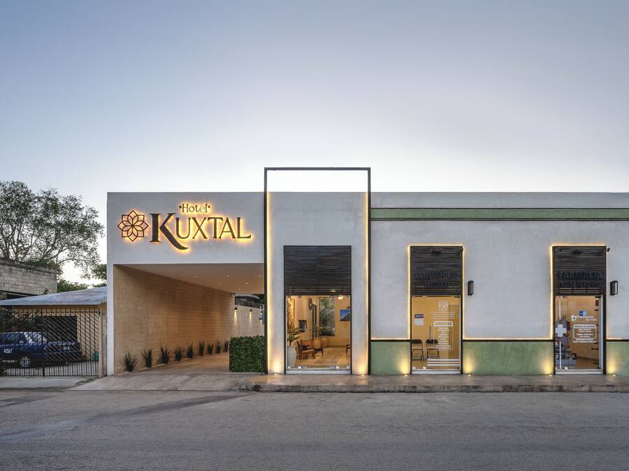 A hotel named "Hotel Kuxtal" with a modern facade, large windows, and a visible entrance.