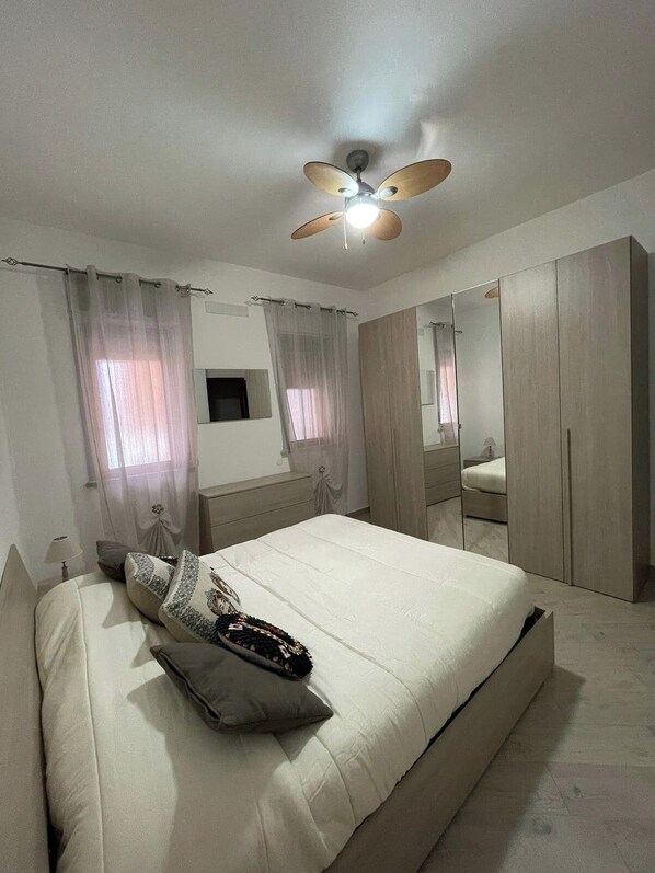 A bedroom with a bed, a ceiling fan, a wardrobe, and a mirror.