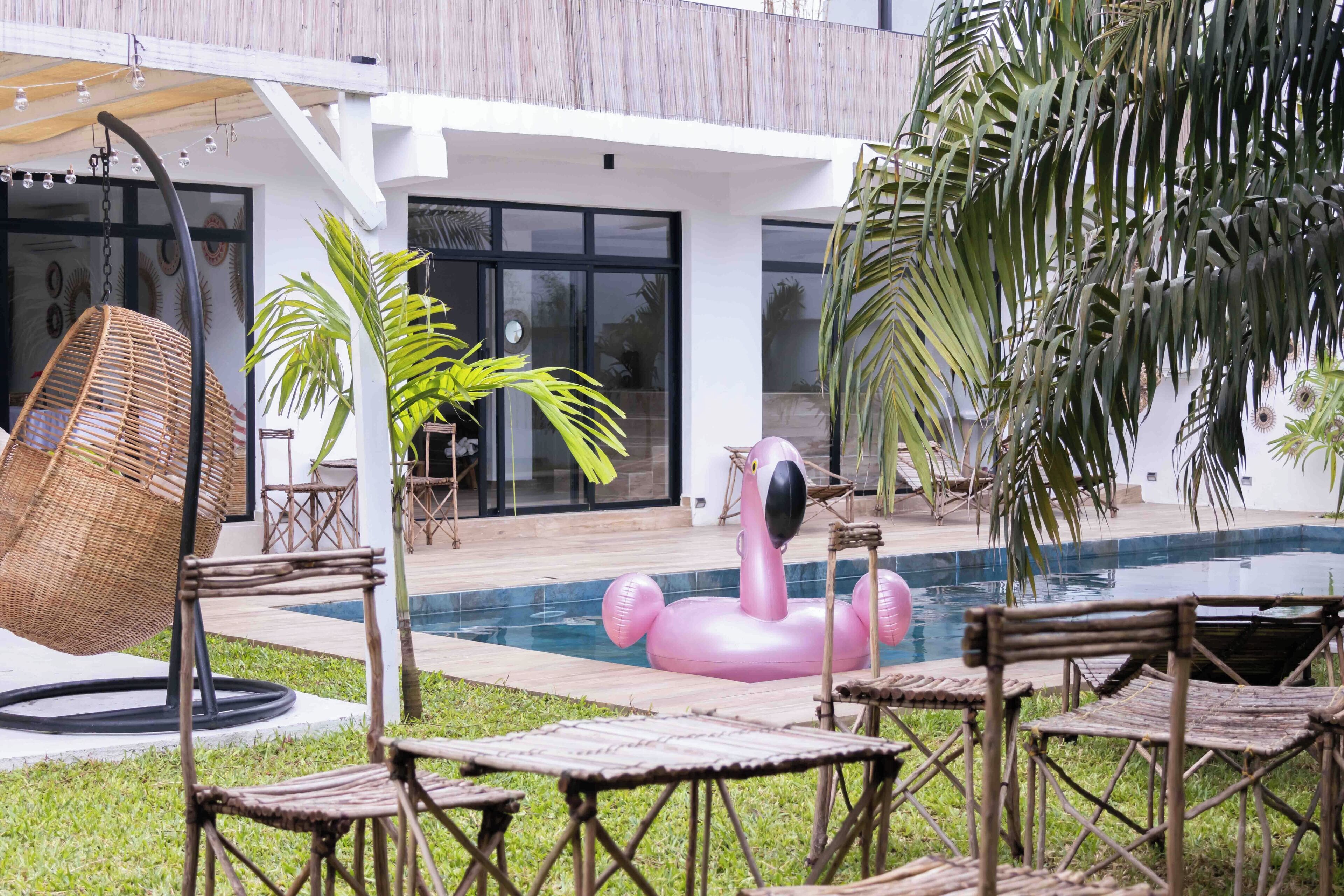 A pool area with a pink flamingo float, wicker chairs, and a hanging chair.