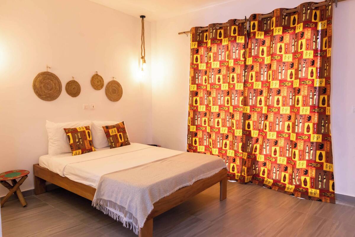 A bedroom with a wooden bed, white bedding, a patterned curtain, and wall-mounted circular decorations.