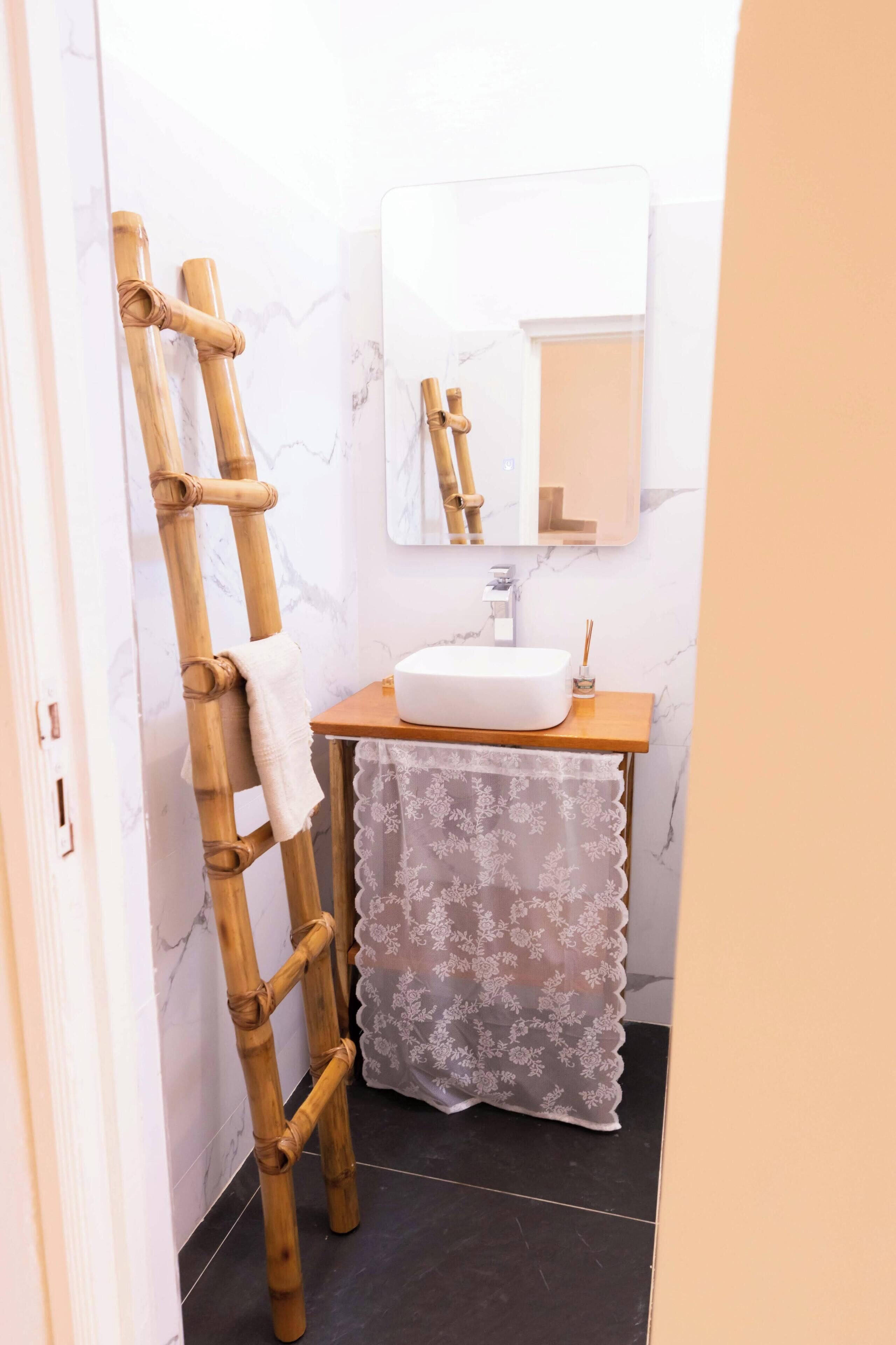 Ein Badezimmer mit einer Holzleiter, einem weißen Waschbecken, einem Spiegel und einem blumigen Vorhang.
