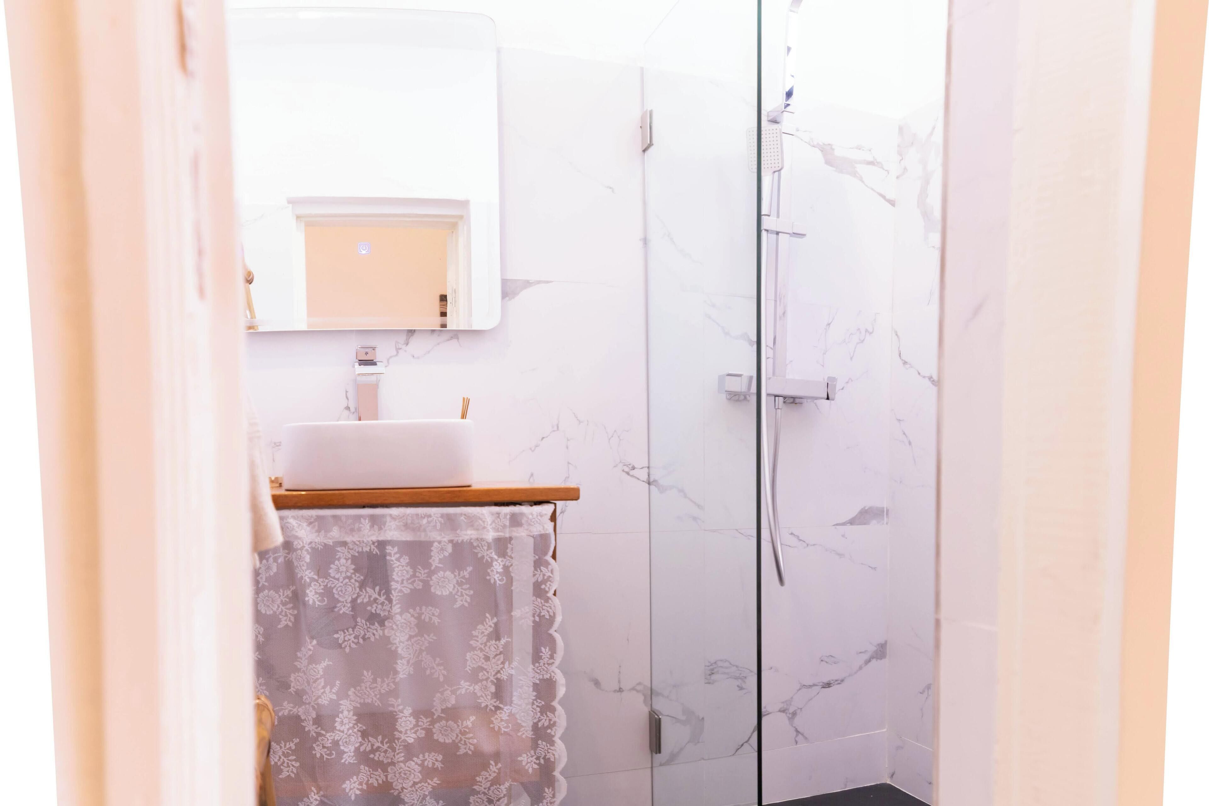 Een badkamer met een marmeren douche, een wastafel en een spiegel.