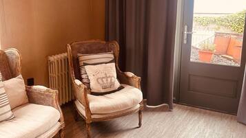 Een kamer met een houten plafond, een groot raam met gordijnen, een deur en twee rieten stoelen met kussens.