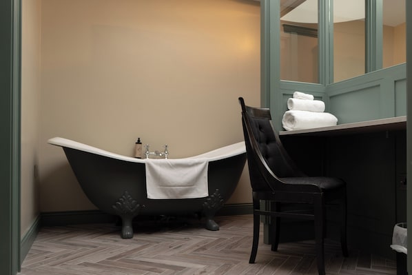 Un baño con una bañera independiente, una silla y un espejo.